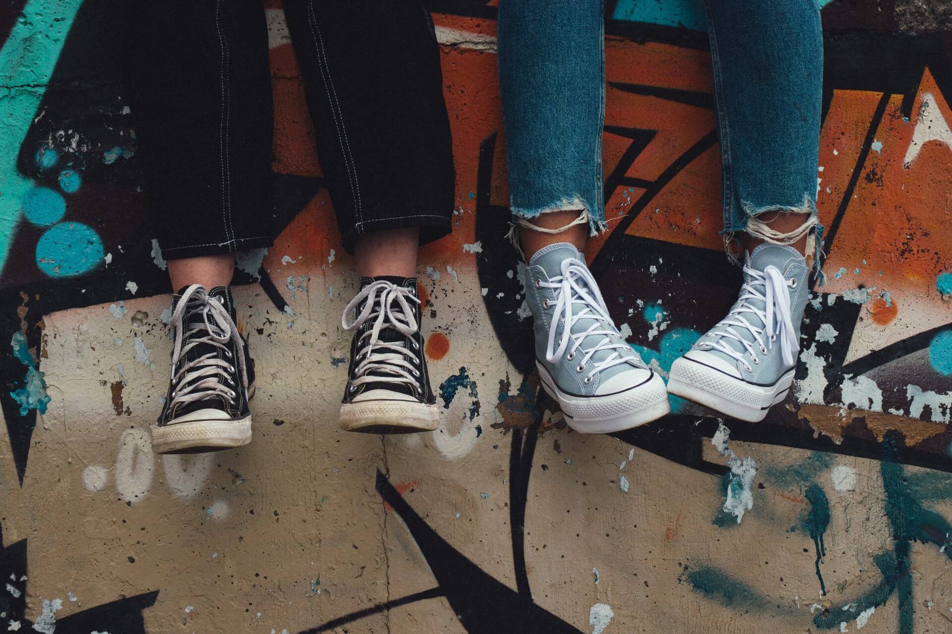 image of the lower legs and feet of two young people wearing jeans and sneakers