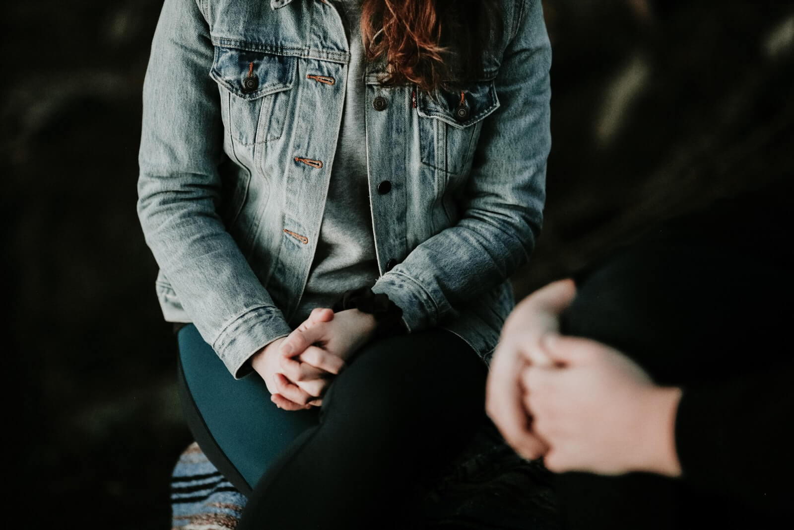 woman wearing gray jacket talking with a second person with hands folded in lap, wearing black clothing.