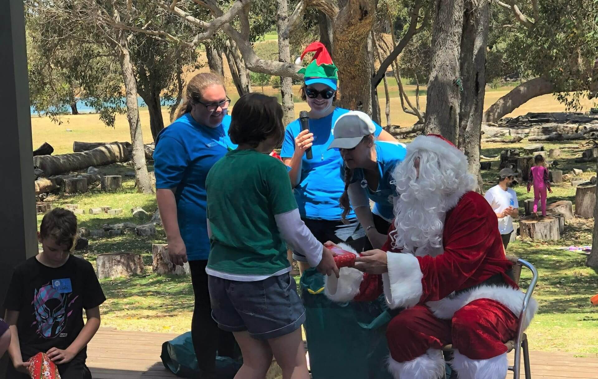 Santa giving a gift to a child at the SWAN Family Christmas Party 2022, assisted by SWAN volunteers.