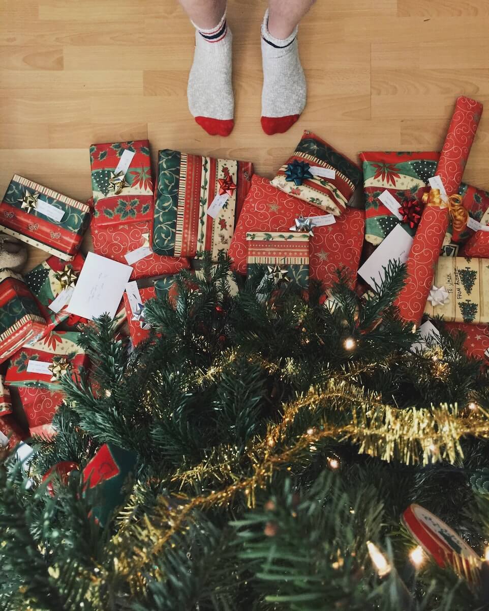 socked feet standing in front of Christmas tree with lots of presents underneath.